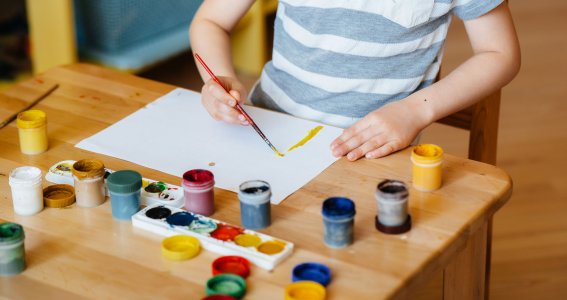 Ein Junge malt mit unterschiedlichen Farbbechern