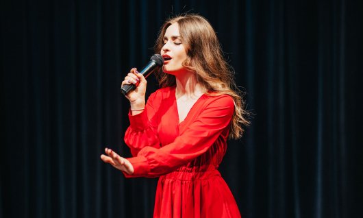 Eine Frau in rotem Kleid sing vor einem dunkelblauen Vorhang