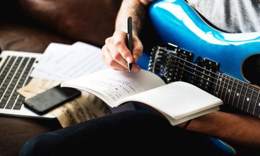 Ein Mann sitzt mit E-Gitarre und schreibt in einen Notizblock