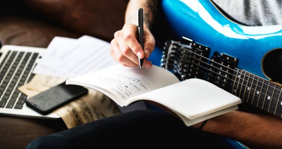 Ein Mann sitzt mit E-Gitarre und schreibt in einen Notizblock