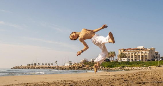 Ein Junge in weißer Hose springt in akrobatischer Pose am Strand