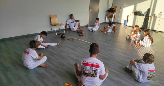 Kinder in Sportkleidung sitzen mit ihrem Trainer im Kreis eines leeren Raumes