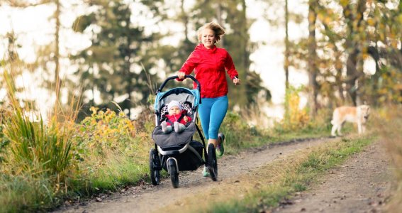 Mama macht mit Baby und Kinderwagen in der Natur Sport.