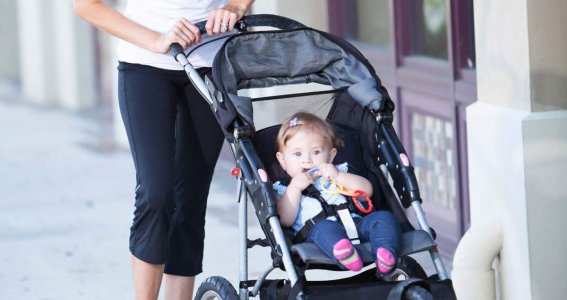 Eine Frau spaziert mit dem Kinderwagen und ihrem Baby.