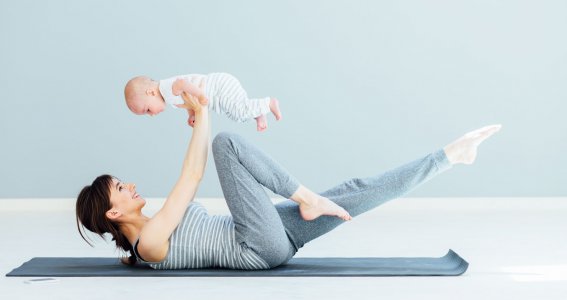 Frau hält ihr Baby beim Sport treiben in die Luft.
