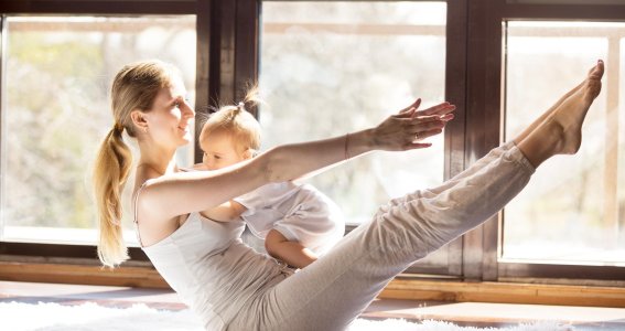 Frau macht Sport mit ihrem Baby auf dem Schoß.