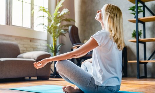 Eine Frau sitzt im Schneidersitz auf einer Yogamatte und meditiert
