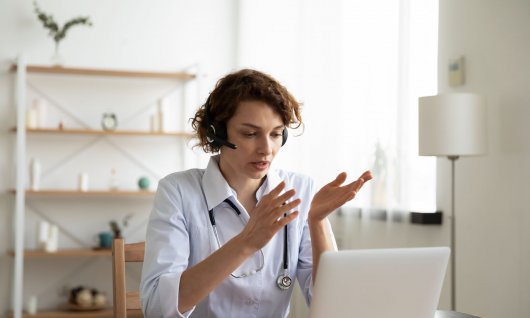 Eine Frau sitzt mit Kopfhörern vor einem Laptop und spricht gestikulierend