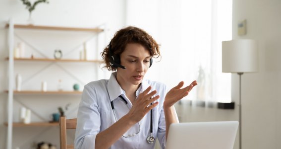 Eine Frau sitzt mit Kopfhörern vor einem Laptop und spricht gestikulierend