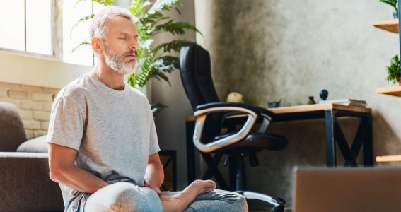 Ein Mann meditiert in einem Arbeitszimmer auf einer Yogamatte