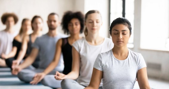 Eine Gruppe von Menschen meditiert nebeneinander auf Yogamatten