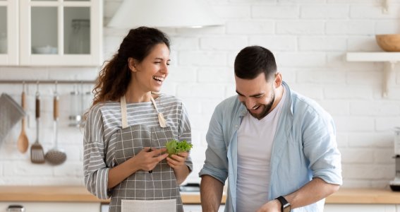 Eine Frau mit Kochschürze und ein Mann schneiden in einer Küche Gemüse und lachen