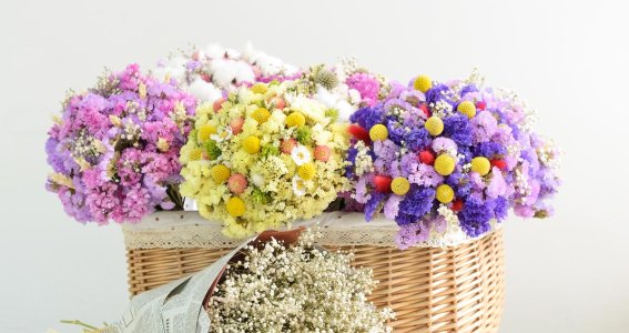 Ein Korb mit unterschiedlich-farbigen Trockenblumen und ein Strauß aus Trockenblumen daneben 