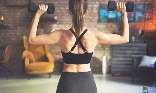 Frau von hinten mit zwei Hanteln in den Händen