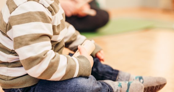 Baby hält eine Holzrassel in der Hand und sitzt auf dem Boden