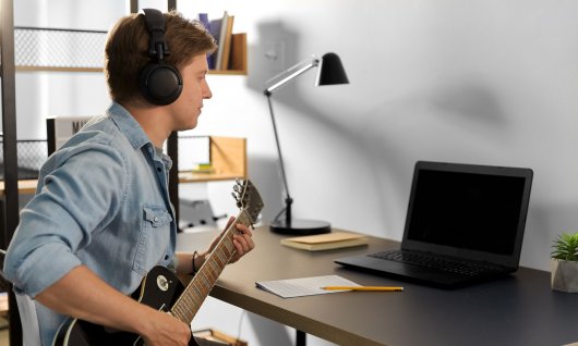 Mann spielt Bass und sitzt vor einem Laptop