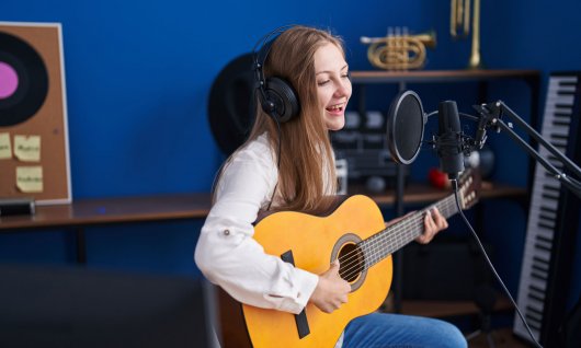 Mädchen spielt Gitarre und singt in ein Mikro 