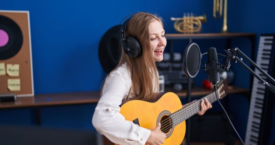 Mädchen spielt Gitarre und singt in ein Mikro 