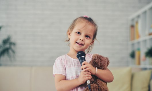Gesangsunterricht für Kinder Mädchen hält Teddybär und Mikrofon
