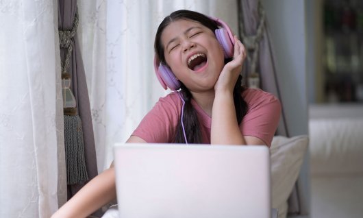 Online Gesangskurs für Jugendliche Mädchen singt mit Kopfhörern vor einem Laptop