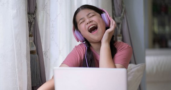 Mädchen singt mit Kopfhörern vor einem Laptop