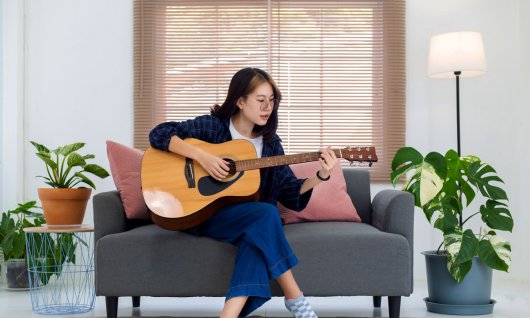 Frau sitzt auf der Couch und spielt Gitarre