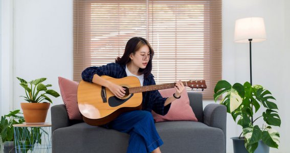 Frau sitzt auf der Couch und spielt Gitarre