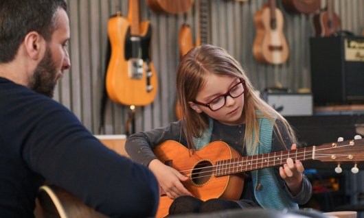 Gitarrenunterricht für Kinder Mädchen mit Brille spielt Gitarre