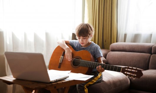 Online Gitarre lernen für Kinder Junge sitzt vor einem Laptop und spielt Gitarre