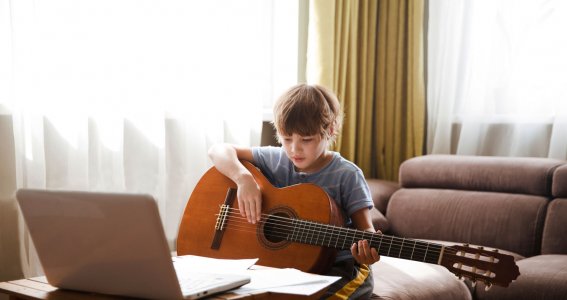 Junge sitzt vor einem Laptop und spielt Gitarre