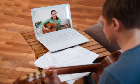 Online Gitarrenunterricht für Erwachsene Person mit Gitarre auf dem Laptopbildschirm