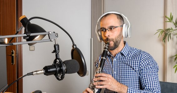 Mann trägt Kopfhörer und spielt Klarinette in ein Mikro