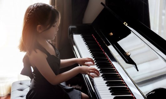 Klavierkurs für Kinder Mädchen sitzt auf einem Hocker und spielt Klavier