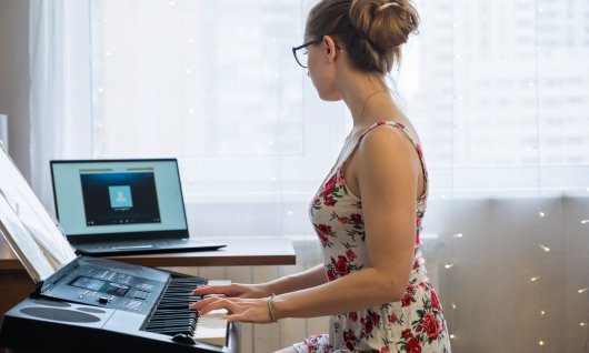 Online Unterricht im Klavier spielen für Jugendliche Jugendliche hat die Hände auf der Tastatur und schaut auf ihren Laptop