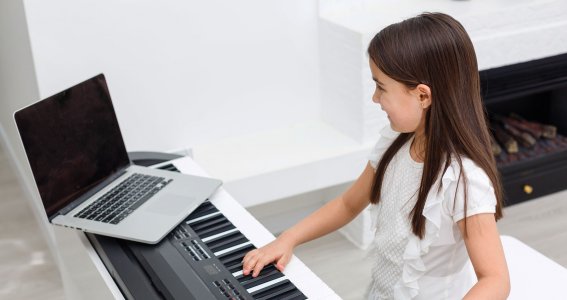 Mädchen schaut auf Laptop während sie auf dem Keyboard spielt
