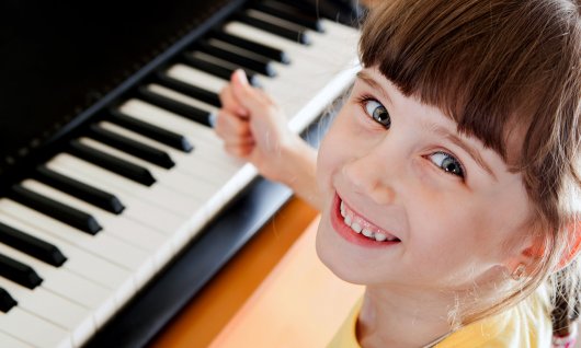Instrumente kennenlernen für Kinder Mädchen sitzt lachend am Klavier