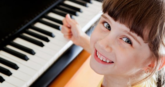 Mädchen sitzt lachend am Klavier
