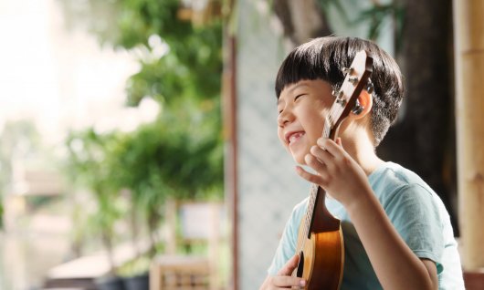 Online Ukulelenunterricht für Kinder Kind lacht mit einer Ukulele
