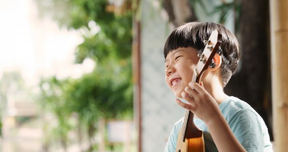 Kind lacht mit einer Ukulele