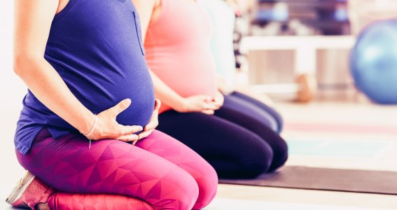 Schwangere in Sportklamotten halten ihren Babybauch