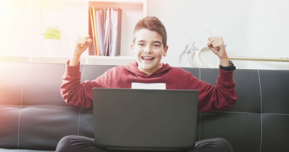 Junge der vor einem Computer sitzt und sich freut