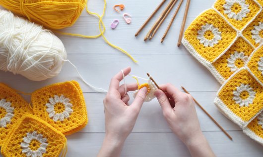 Zwei Hände häkeln gelb weise Stücke