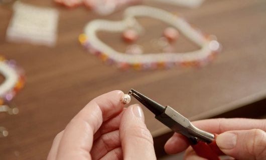 2 Hände mit  Zange und einer Perle 