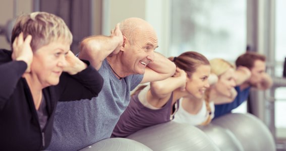 Eine Gruppe Erwachsener balancieren auf Yogabällen und lehnen sich mit den Händen hinter den Köpfen nach hinten