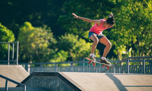 Eine junge Frau im Skatepark versucht einen Skateboard-Trick