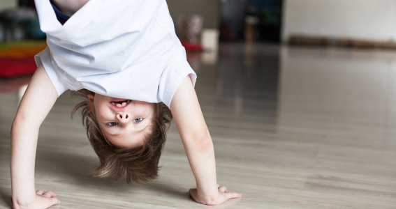 Ein kleiner Junge in weißer Capoeira-Trainingskleidung ist kopfüber in einem leeren Raum