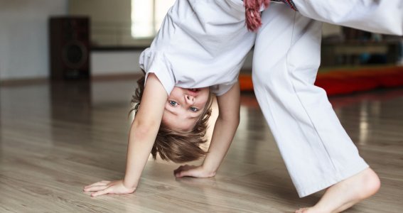 Ein kleiner Junge setzt in weißer Capoeira-Trainingskleidung zum Rad an