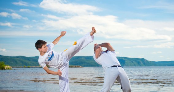 Ein Junge trainiert mit einem Mann in weißer Kleidung Capoeira am Strand