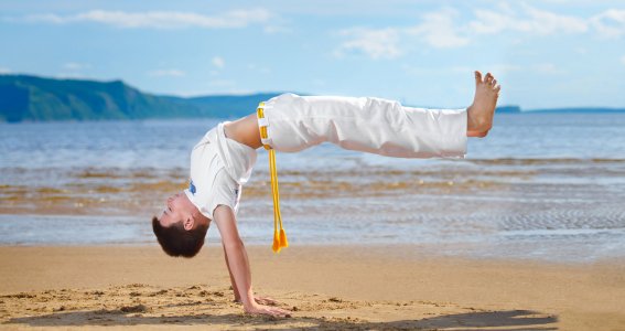 Ein Jugendlicher macht am Strand eine Capoeira-Pose