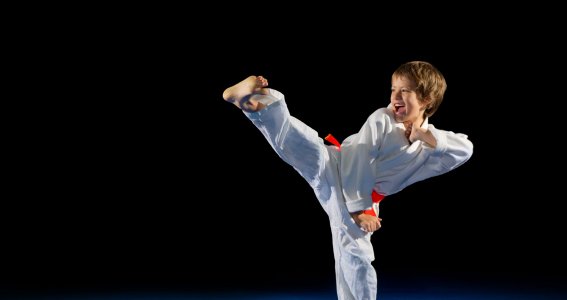 Ein Junge in Taekwondo-Anzug übt einen Fußtritt vor schwarzem Hintergrund